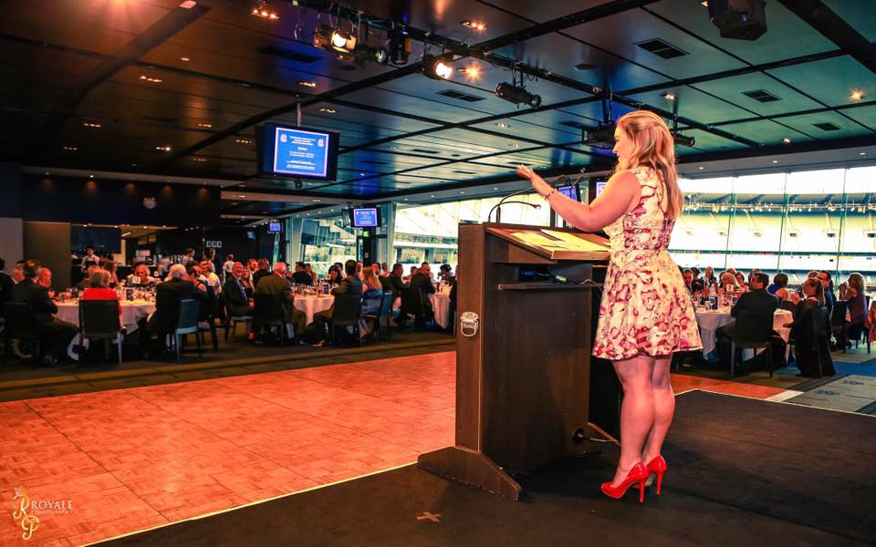 Jodie Coall speaking from a podium to a room of business owners
